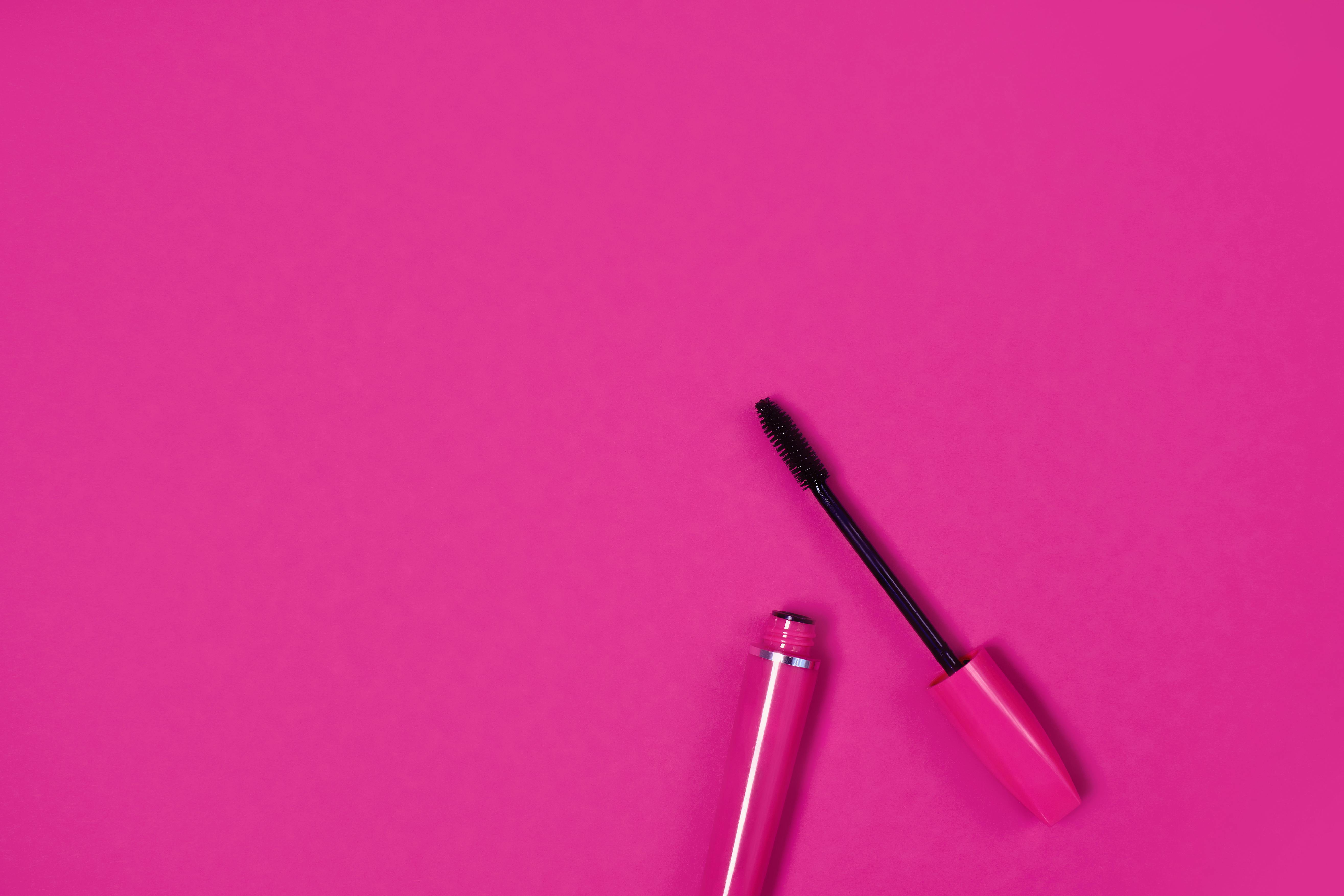 Close-up of an open mascara on a bright pink background, perfect for beauty and fashion themes.