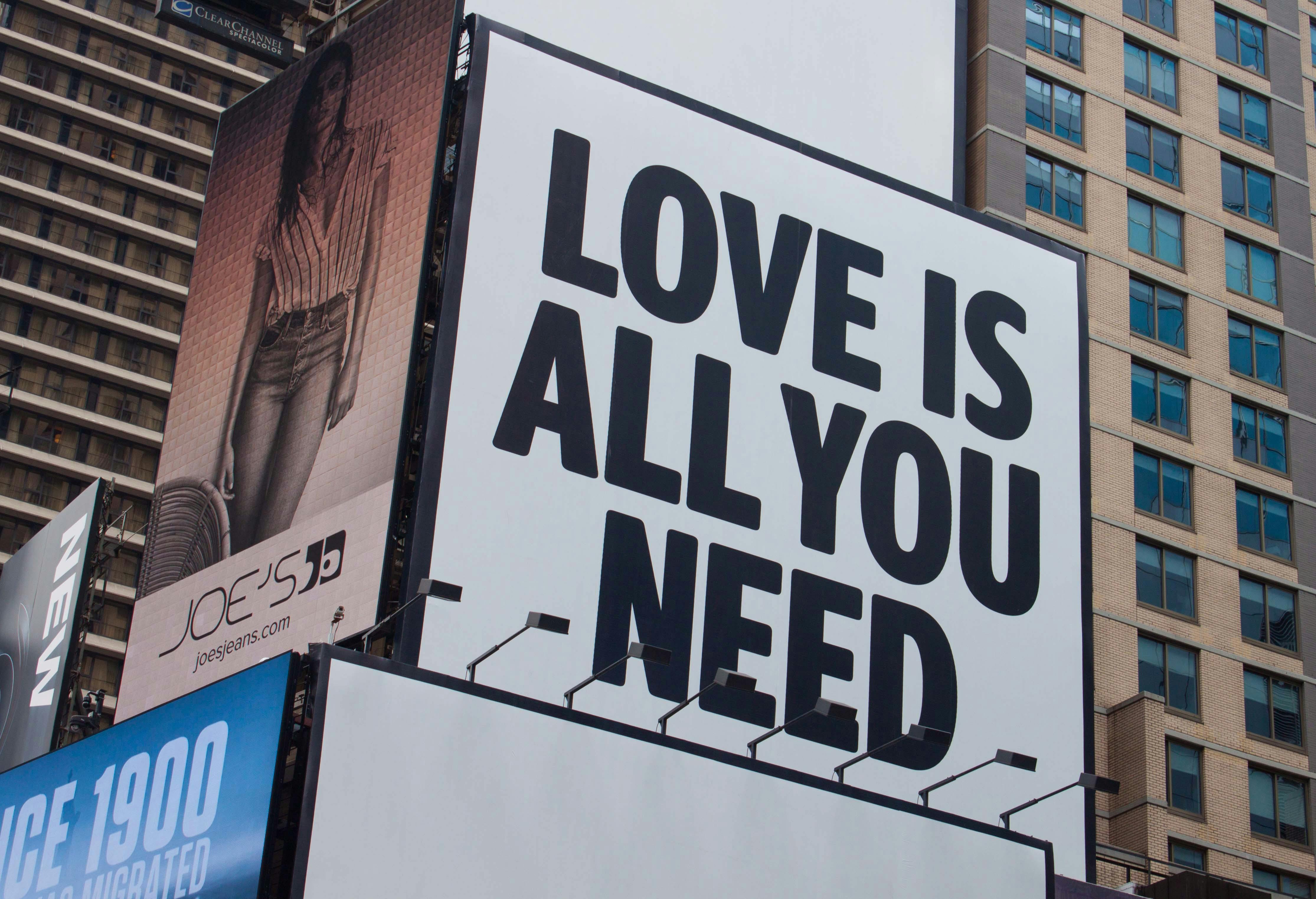 Large city billboard reads 'Love Is All You Need' in New York City street.
