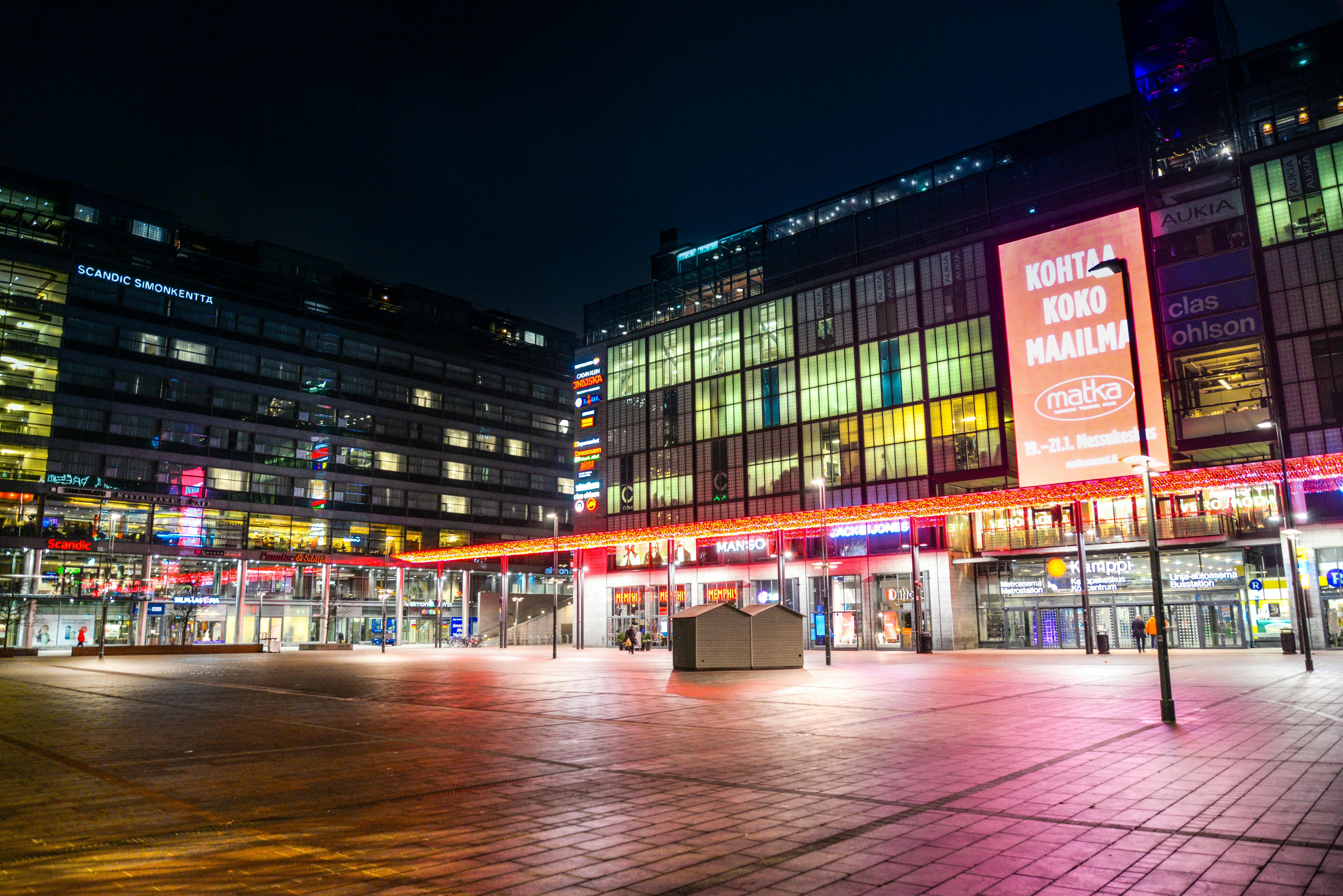 Illuminated city square at night showcasing modern architecture and vibrant signage.